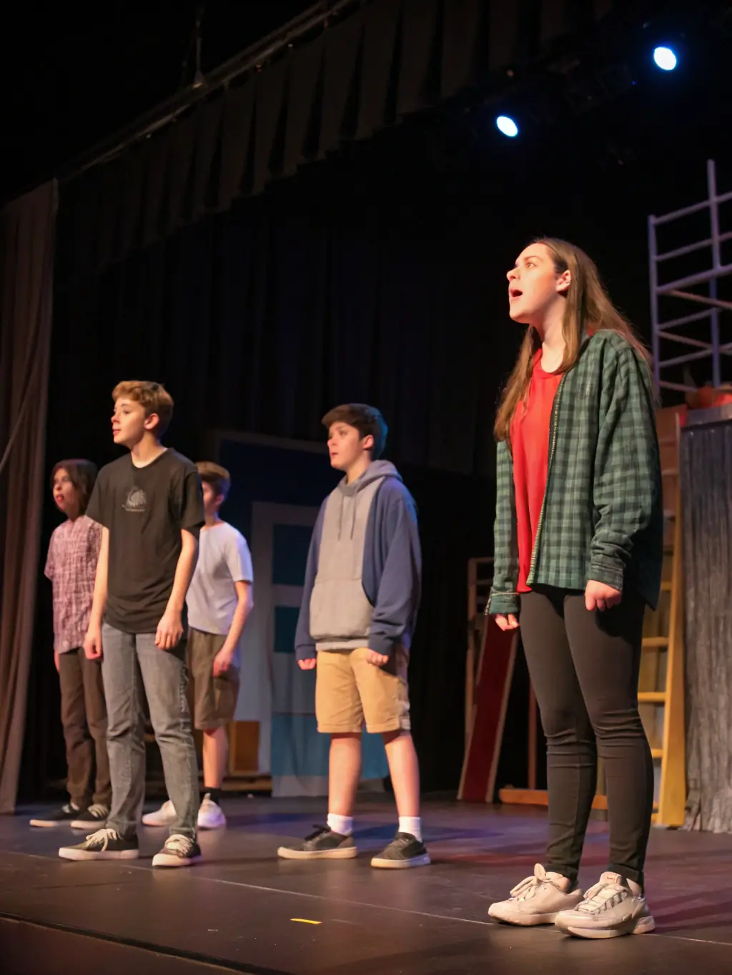 A group of teenagers participating in a drama workshop, rehearsing a scene with enthusiasm and teamwork, highlighting the performing arts aspect of the Cultural and Artistic Workshops.